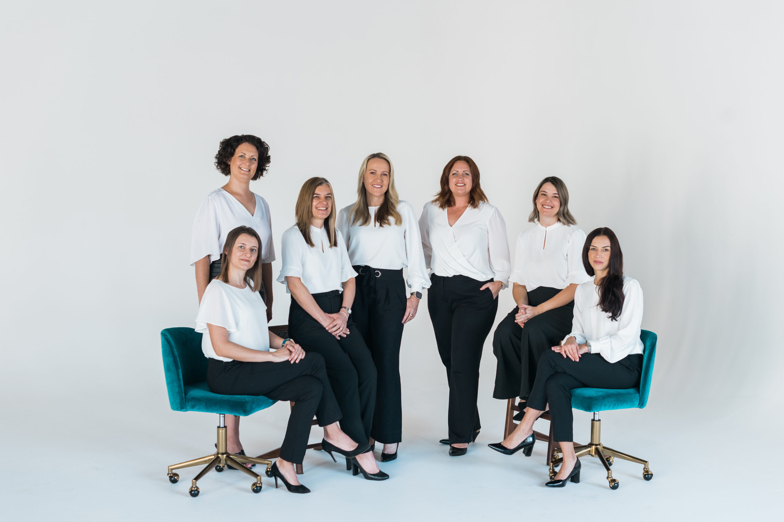 Team of women, some sitting on teal velvet chairs.