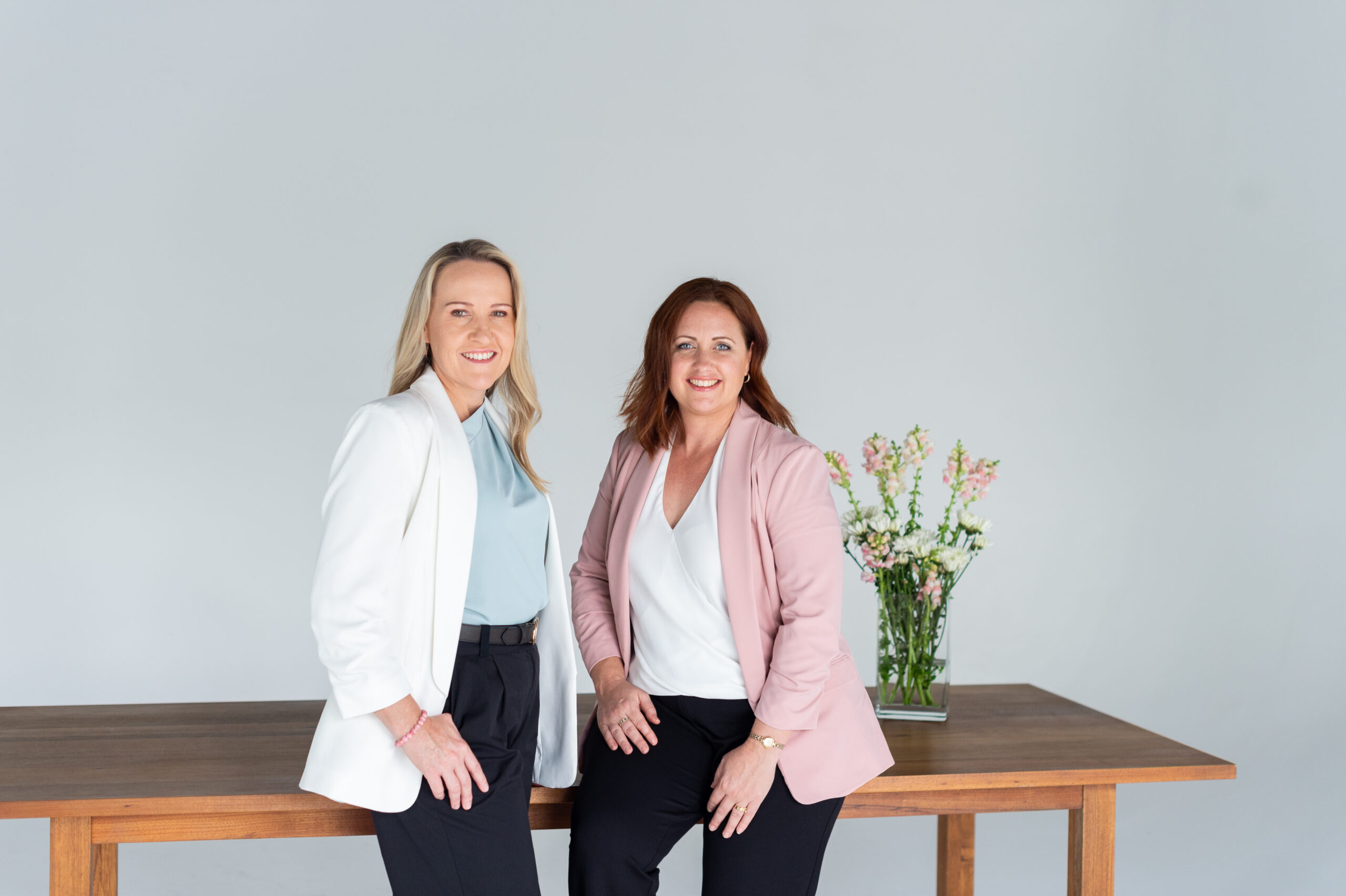 Lisa Carter & Jen Bettridge of Clear Insurance sitting on a desk.